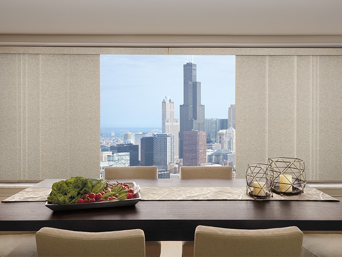 A dining table with large and tall windows featuring Skyline® Gliding Window Panels; Fabric: Edinburgh  Color: Cobblestone Paths
